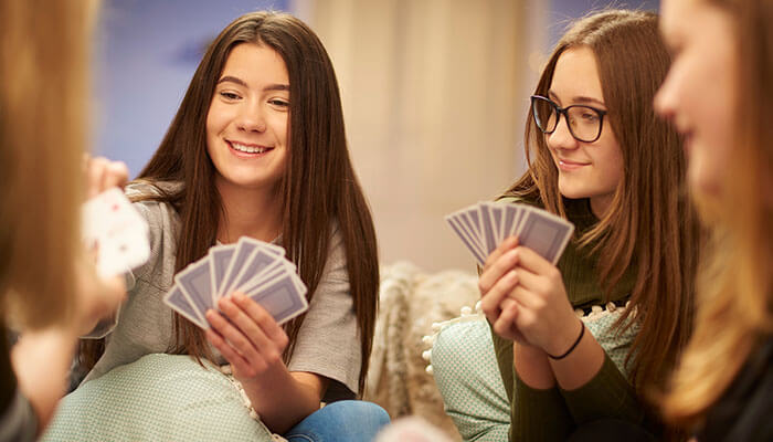 Group of friends enjoying a card game, smiling while holding cards, showcasing the fun and strategy involved in how to play BS (Bullshit).