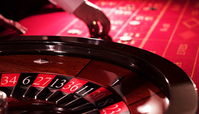 Midnite casino roulette wheel with red and black numbered slots, and a dealer’s hand on the red betting table, showcasing the exciting atmosphere of Midnite’s gaming experience.