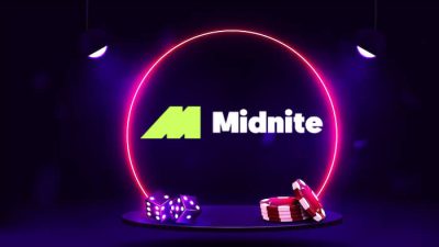 A dark-themed gaming scene featuring a glowing neon pink circular frame with the 'Midnite' logo in the center. Below the logo, there are purple dice and red poker chips displayed on a round platform, illuminated by two overhead spotlights.