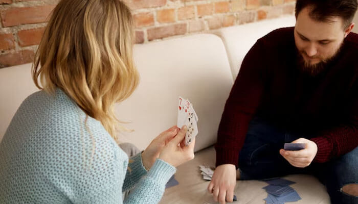 Two players sitting on a couch playing cards, following hand and foot card game rules.