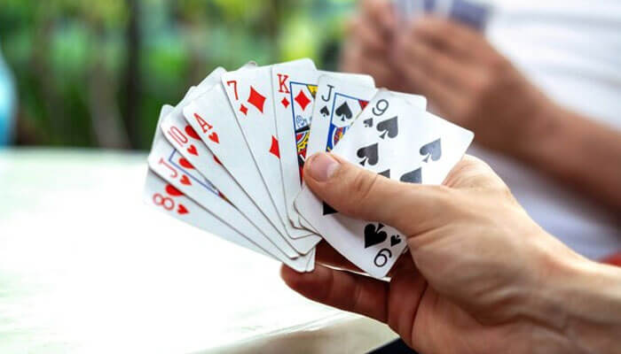 Player holding a fan of cards while playing, demonstrating hand and foot card game rules.