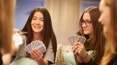 Group of Gen Z friends laughing and playing cards together indoors — enjoying funny card games for Gen Z at a weekend hangout.