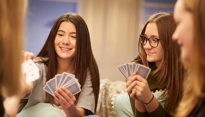 9 Funny Card Games For Gen Z To Play With Others - Live Casino Magic - Live CasinoMagic Group of Gen Z friends laughing and playing cards together indoors — enjoying funny card games for Gen Z at a weekend hangout.