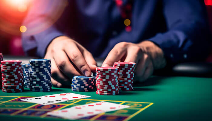 Player stacking poker chips and playing cards on a green casino table at Planet 7 Casino under bright lights.