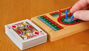 Cribbage board with pegs in play, next to a deck of cards, illustrating the setup for a game of Cribbage and its scoring system