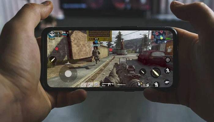 Mobile Gaming - Live Casino Magic - Live CasinoMagic Games Techoelite mobile gaming experience showing a player holding a smartphone with a first-person shooter game, touchscreen controls, and multiplayer action.